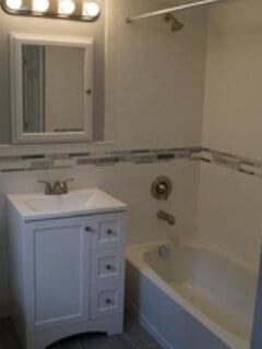corner view of the bathtub, sink cabinet and mirror